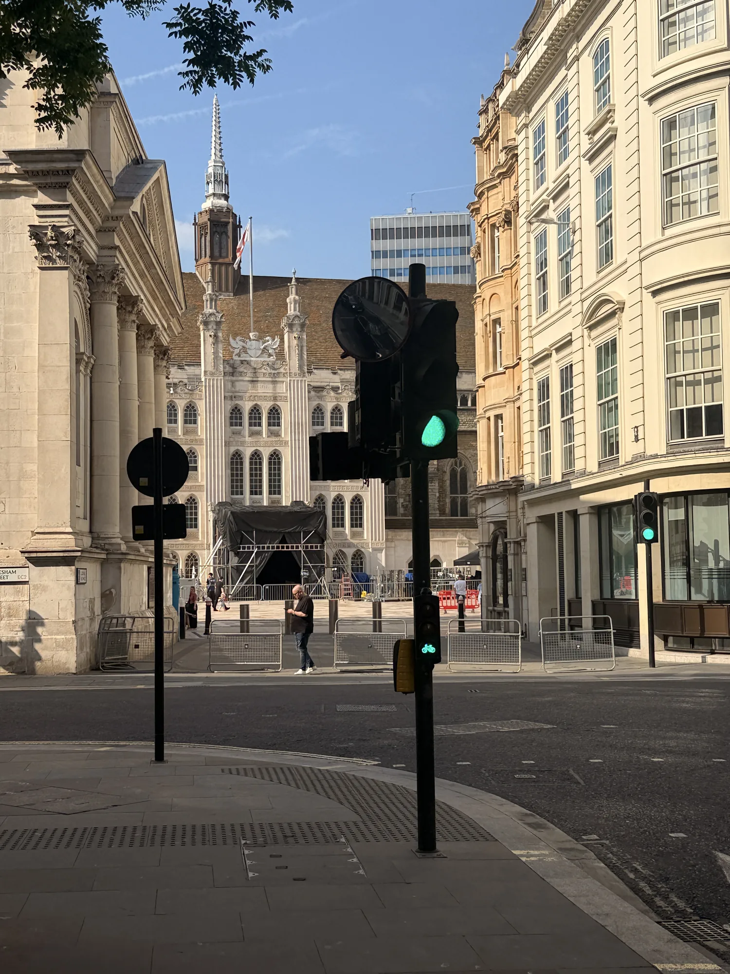 A City of London street with pale stone façades, traffic lights and a spire beneath a blue sky.