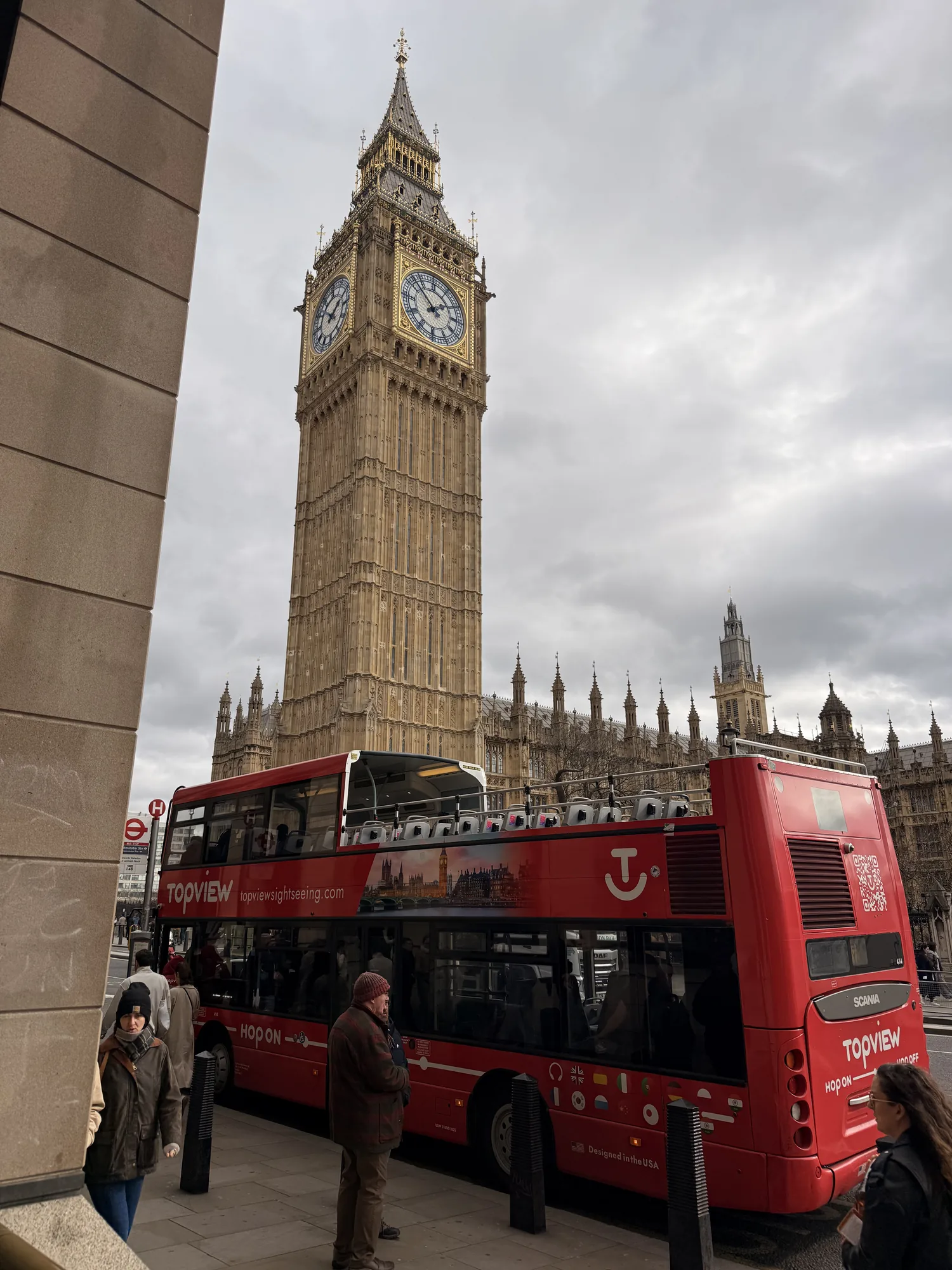 Clock tower, red bus and pale stone beside Westminster in London.