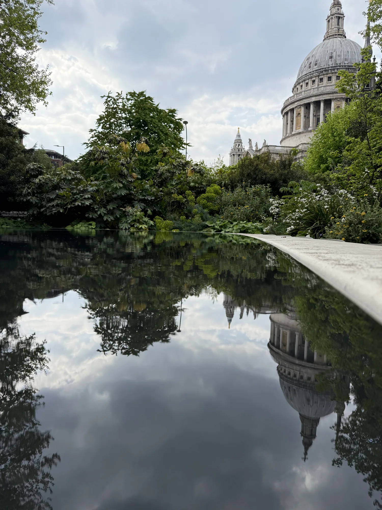 St Paul’s dome reflected in still water beside trees in the City of London.