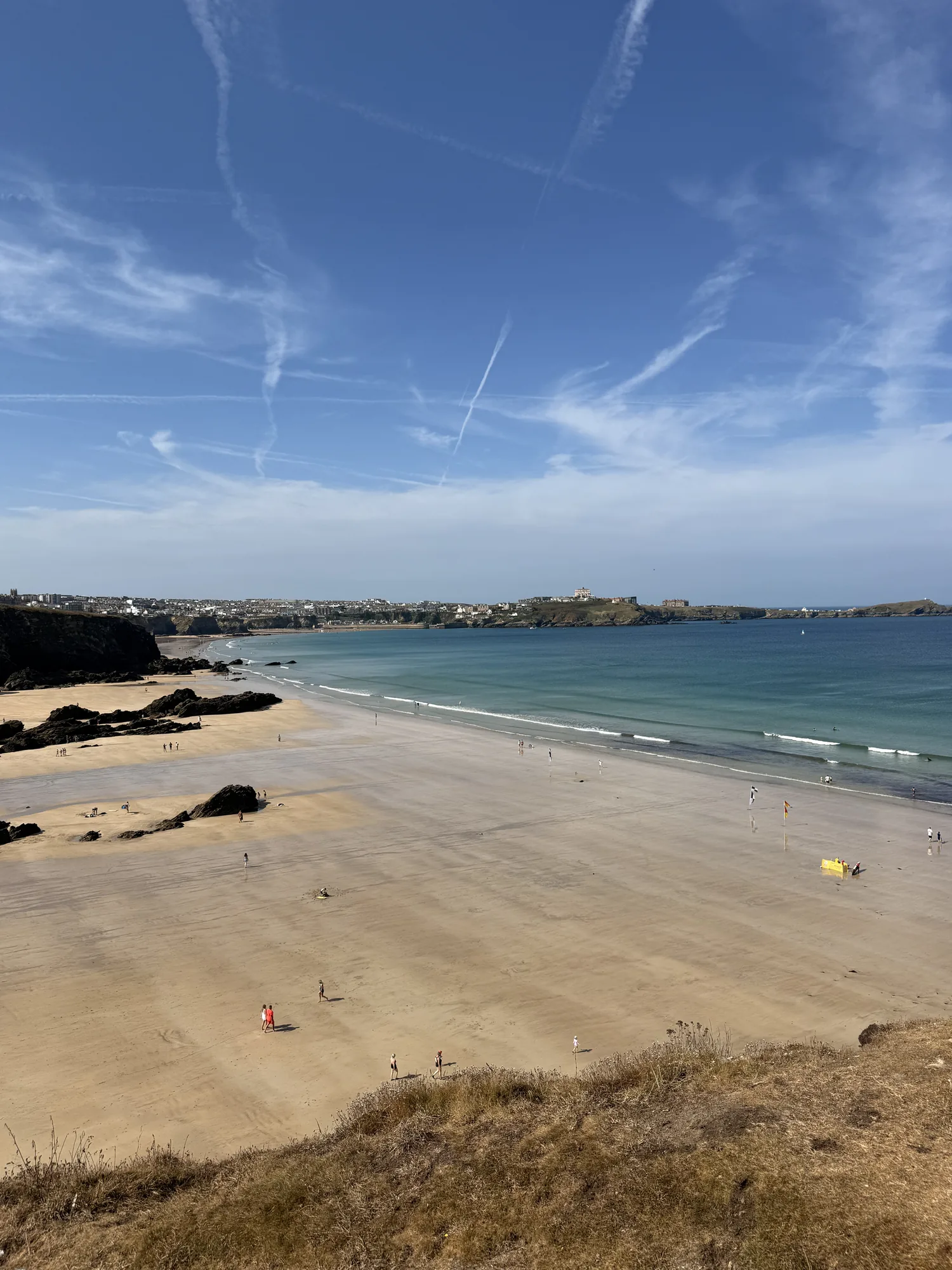 A wide Cornish sandy beach and pale blue water beneath streaked clouds.