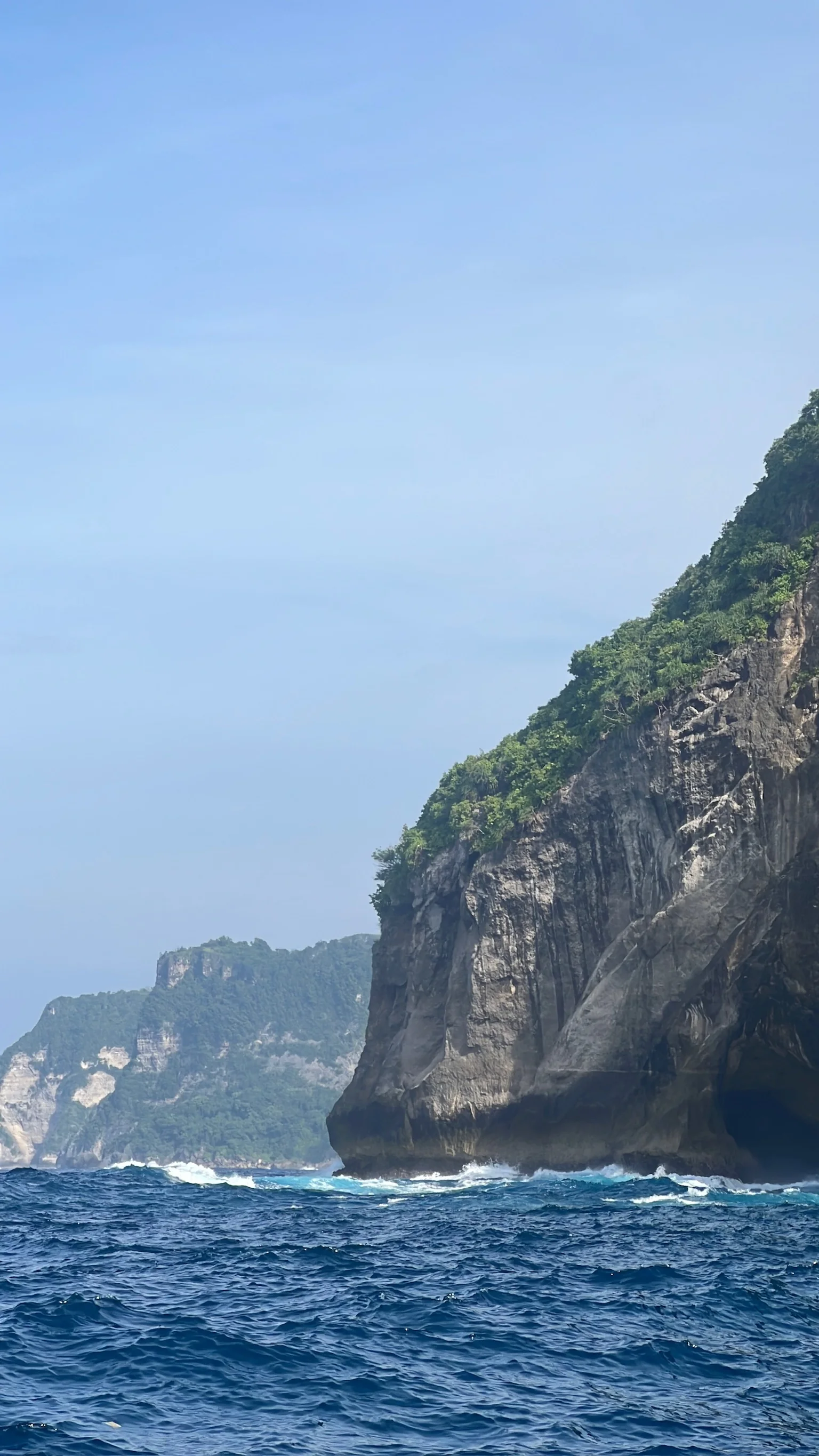 Tall Nusa Penida cliffs above blue sea, photographed from the water
