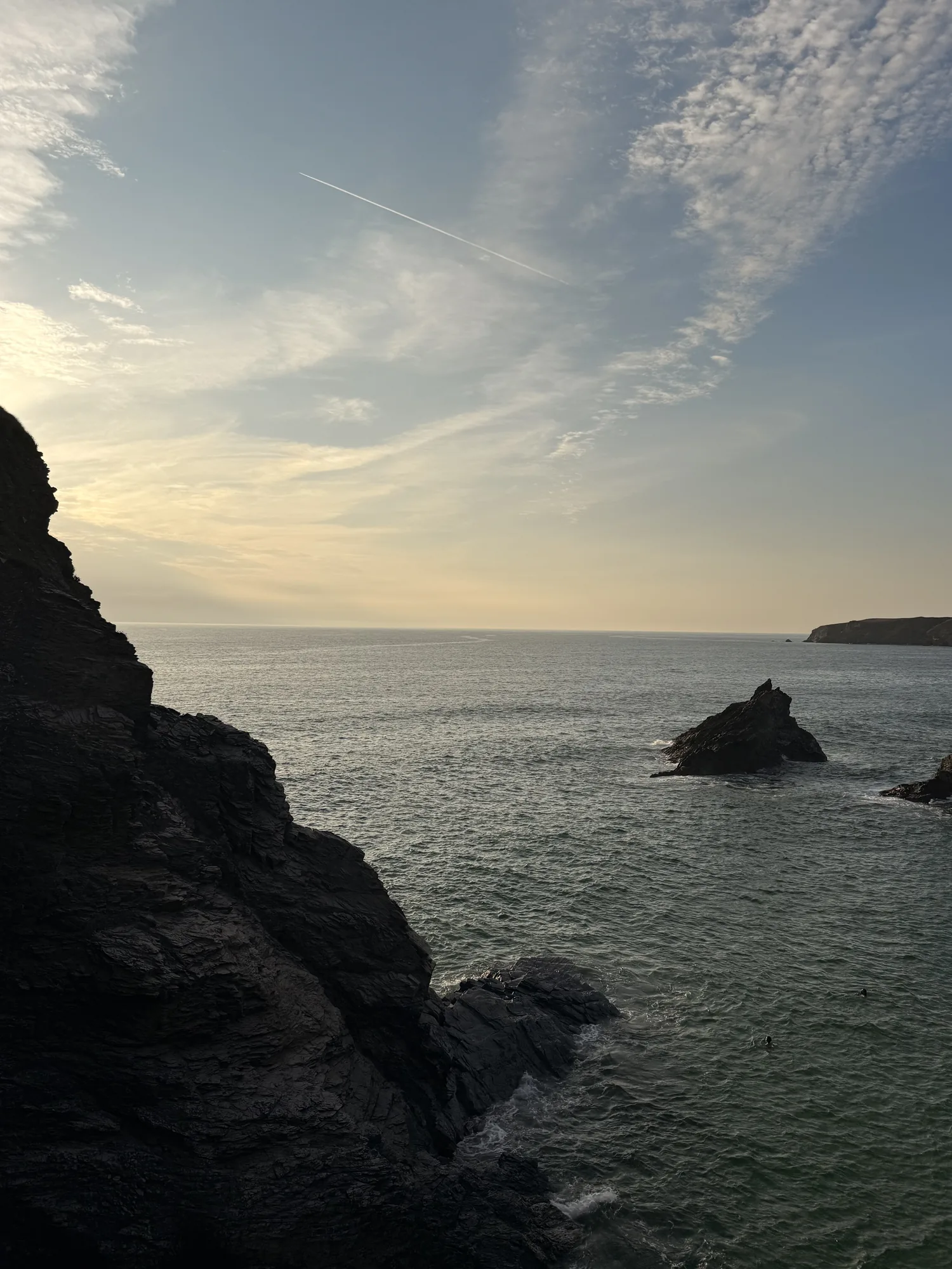 Low evening light across water and dark coastal rock in Cornwall.