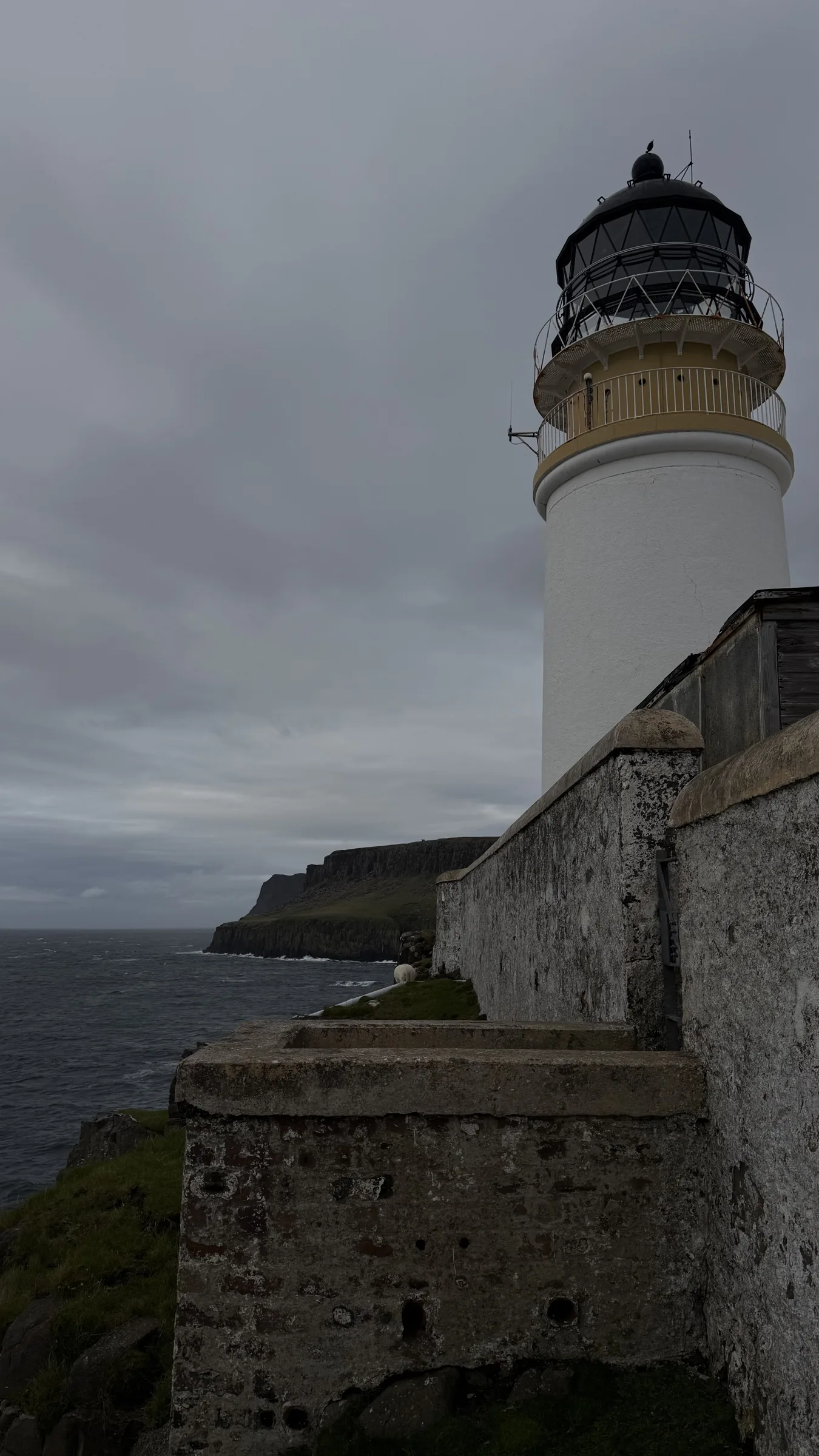 White lighthouse above a stone wall at Neist Point on Skye