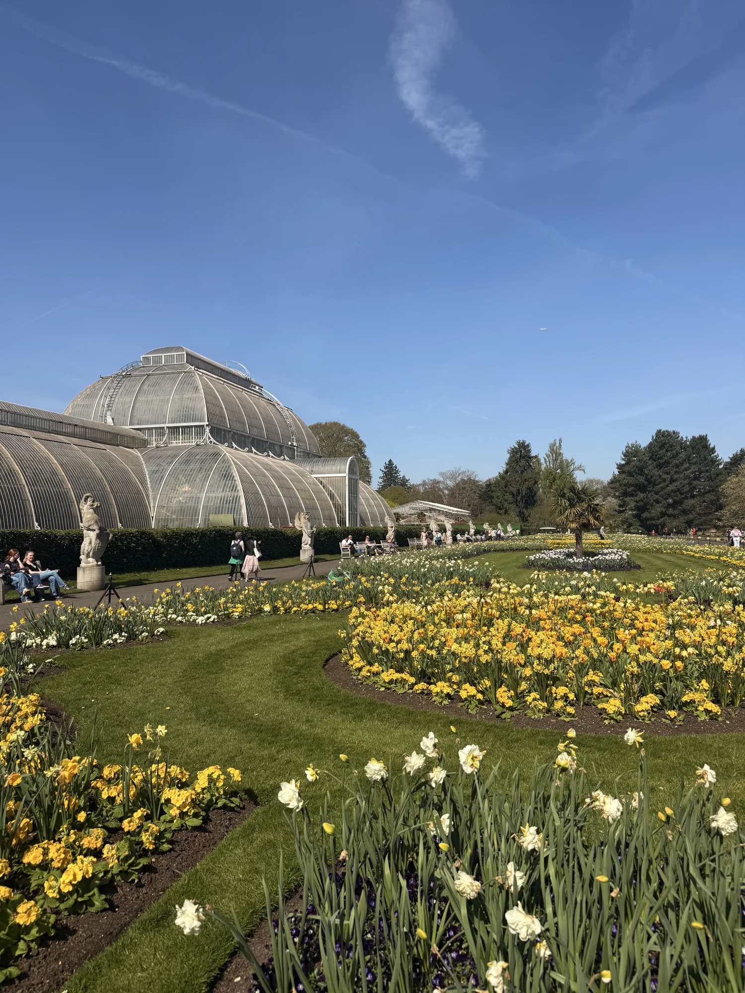 Kew’s Palm House beyond spring flowers and a wide garden path.