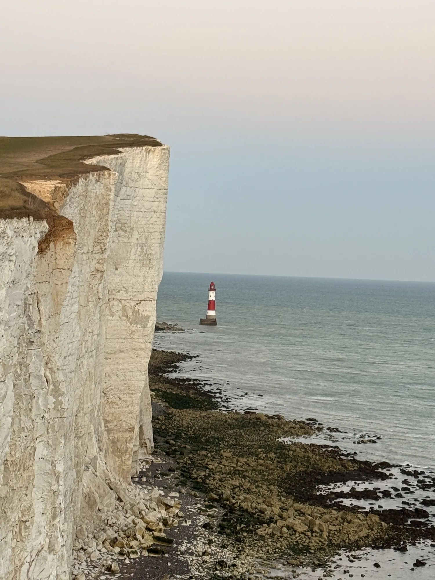 Pale chalk cliffs and the Beachy Head lighthouse in soft evening light.