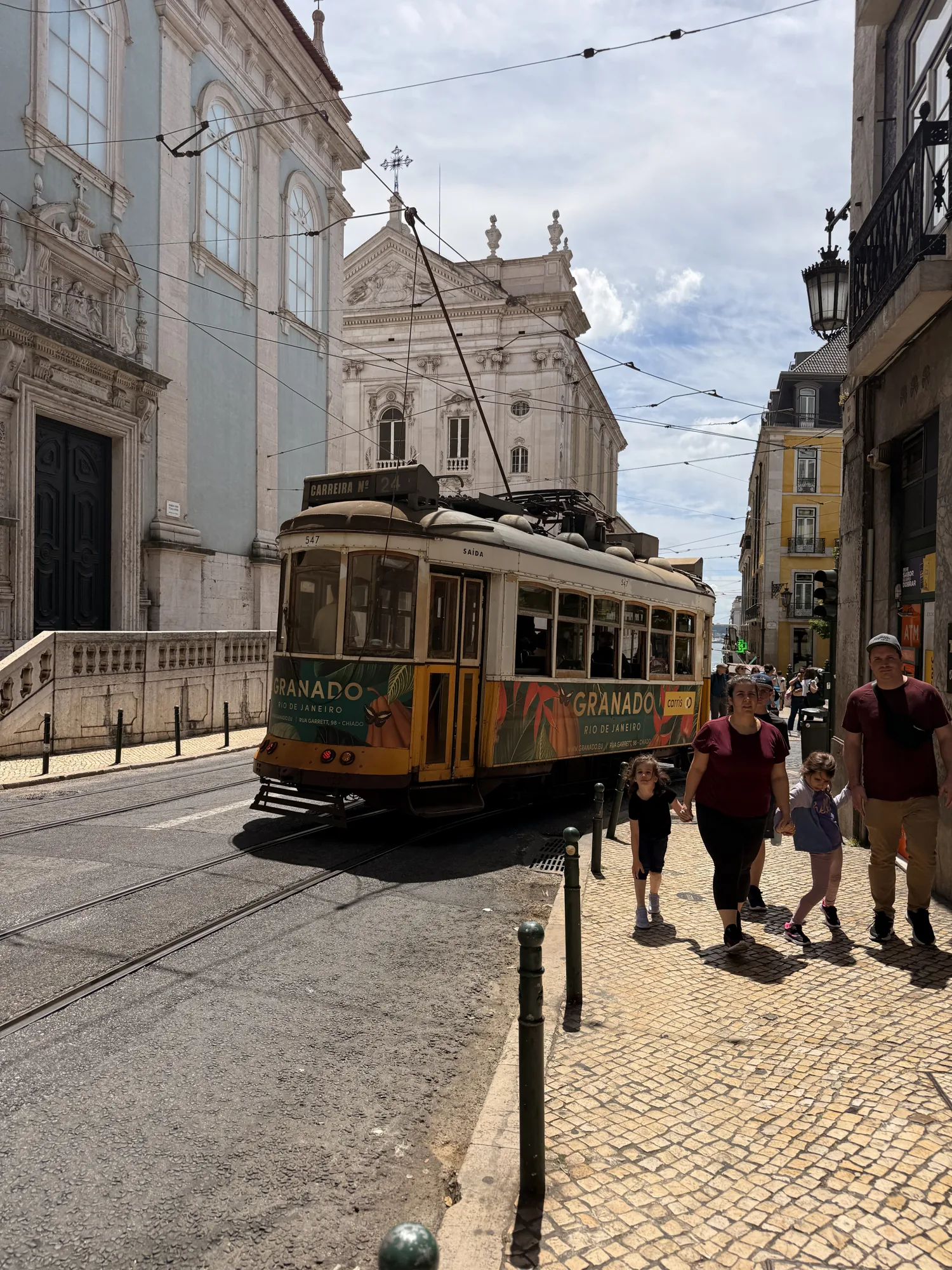Yellow Lisbon tram beside a church facade and stone paving